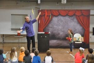 Magician with girl helping entertains young audience